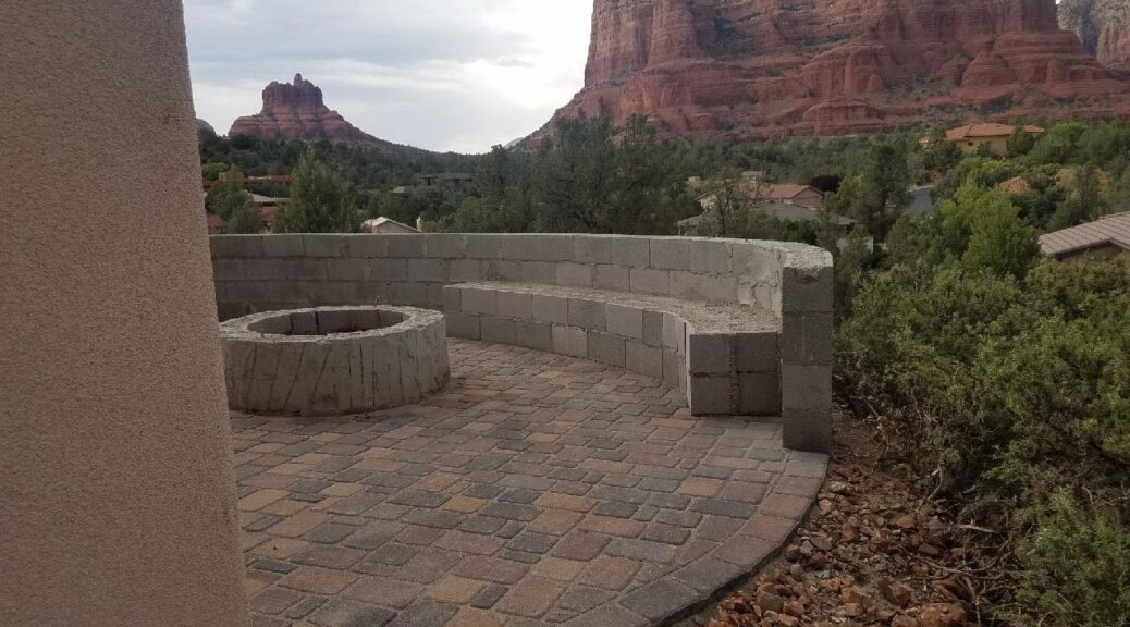 Stone fireplace and seating area in a backyard with Sedona red rocks behind.
